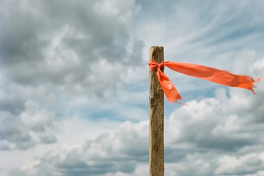 An orange fabric wind flag streams from a wooden stake against a stormy sky above a deflated inflatable.